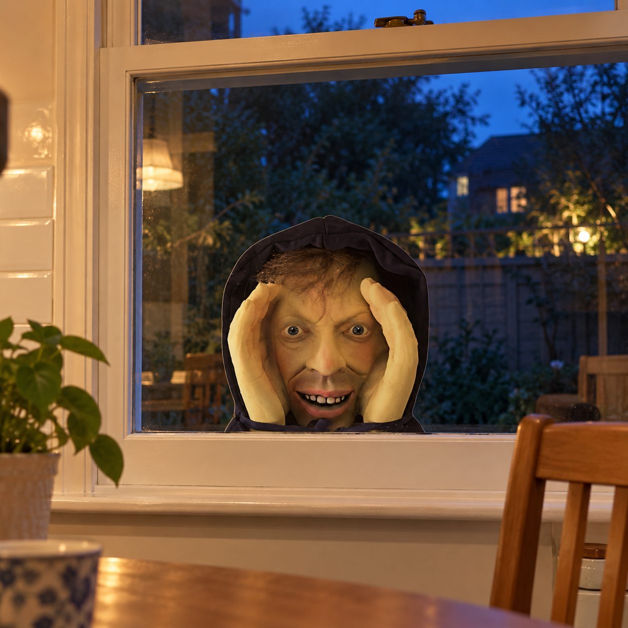 PeepCreep printed face placed low in a kitchen window at dusk